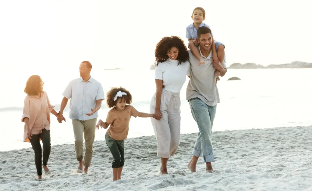 A multi-generational family enjoying a walk on the beach, with children playing and adults chatting, during a warm sunset.